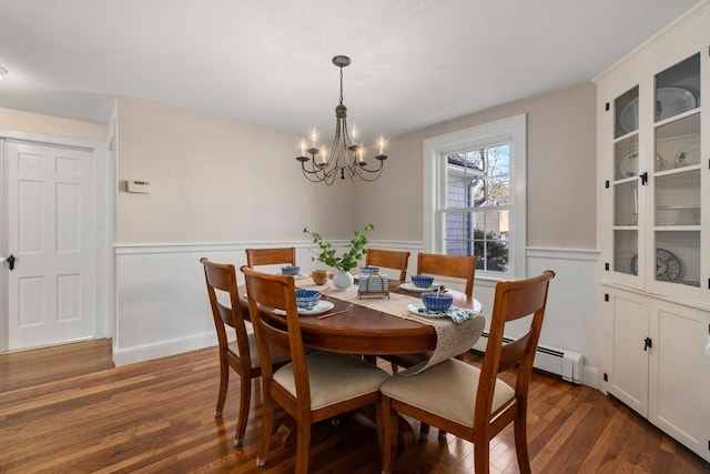 dining space featuring dark wood-style floors, a notable chandelier, a baseboard heating unit, and a wainscoted wall