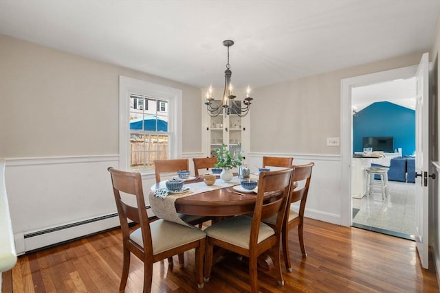 dining room featuring a wainscoted wall, wood-type flooring, a baseboard radiator, and an inviting chandelier