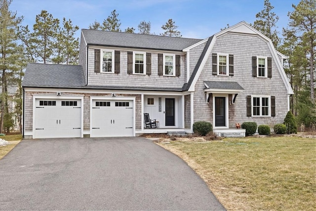 shingle-style home with a front yard, a gambrel roof, driveway, and roof with shingles