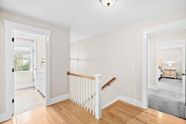 corridor with baseboards, an upstairs landing, and light wood-style floors