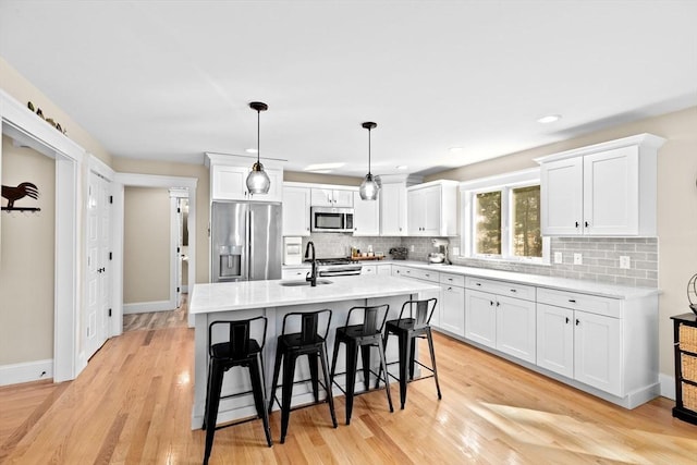 kitchen featuring a breakfast bar, light wood-type flooring, light countertops, appliances with stainless steel finishes, and white cabinetry