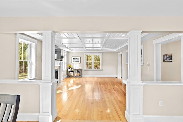 interior space with decorative columns, baseboards, a fireplace, and light wood finished floors