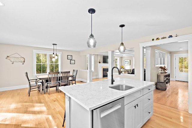 kitchen featuring a glass covered fireplace, light wood-style flooring, a sink, stainless steel dishwasher, and open floor plan