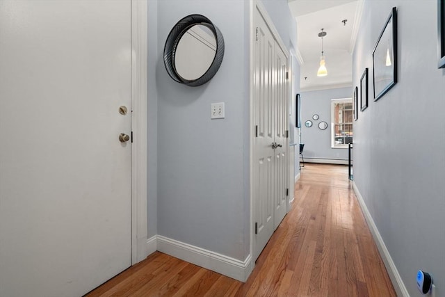 hall with a baseboard heating unit, ornamental molding, and light wood-type flooring