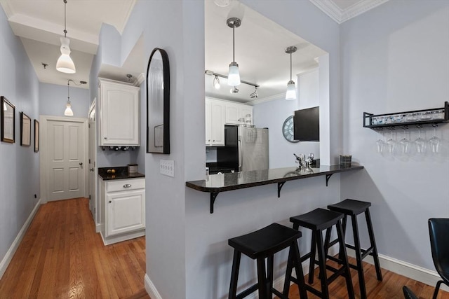 kitchen featuring decorative light fixtures, white cabinetry, kitchen peninsula, stainless steel refrigerator, and a breakfast bar