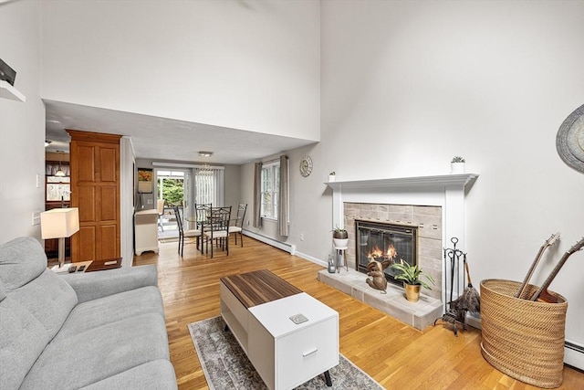 239 Upper County Rd, Dennis, MA 02660 - living area featuring baseboard heating, a towering ceiling, light wood-style floors, a baseboard radiator, and a tiled fireplace