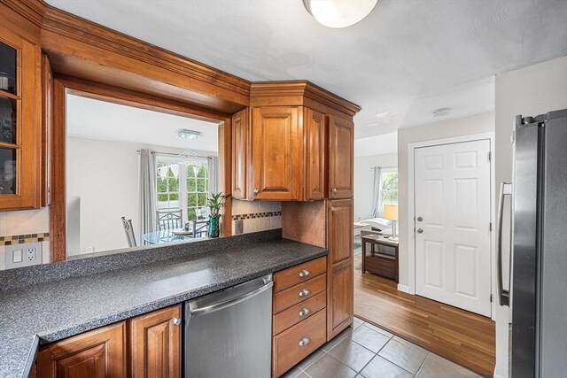 239 Upper County Rd, Dennis, MA 02660 - kitchen with stainless steel appliances, brown cabinetry, tile patterned flooring, and decorative backsplash