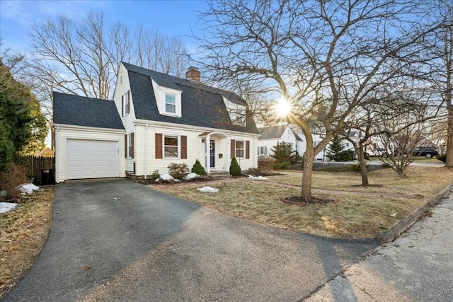 dutch colonial with a gambrel roof, aphalt driveway, roof with shingles, an attached garage, and a chimney