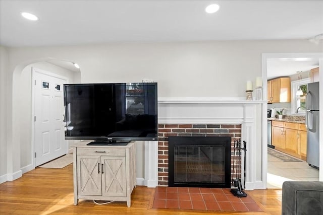 living area with arched walkways, recessed lighting, light wood finished floors, and a brick fireplace