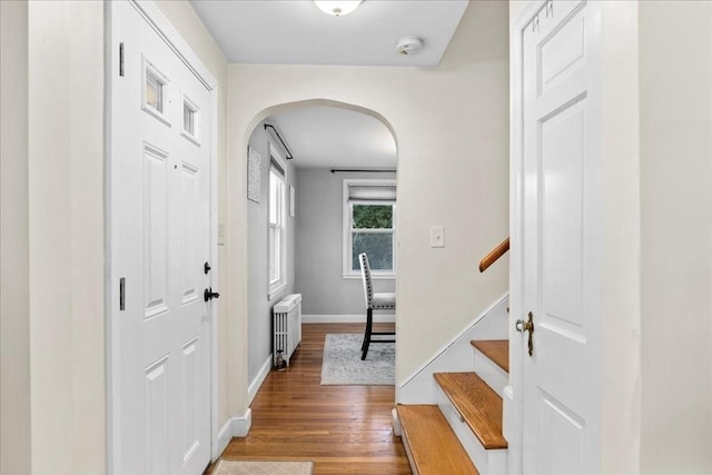 foyer entrance with stairway, wood finished floors, baseboards, radiator heating unit, and arched walkways