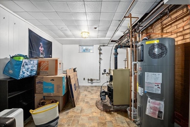 basement featuring stone finish floor, a drop ceiling, water heater, and brick wall