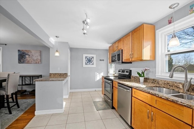 kitchen with brown cabinetry, appliances with stainless steel finishes, dark stone counters, and a sink