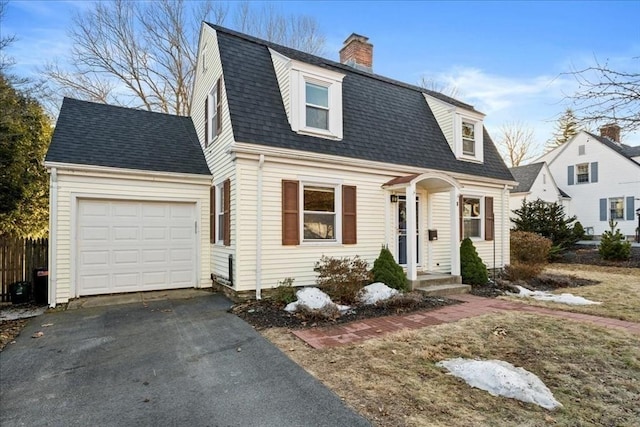 colonial inspired home with an attached garage, a gambrel roof, a chimney, a shingled roof, and aphalt driveway