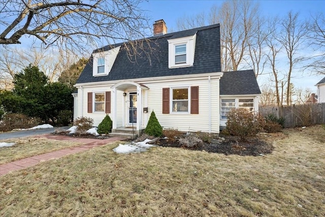 dutch colonial featuring a front lawn, fence, roof with shingles, and a chimney