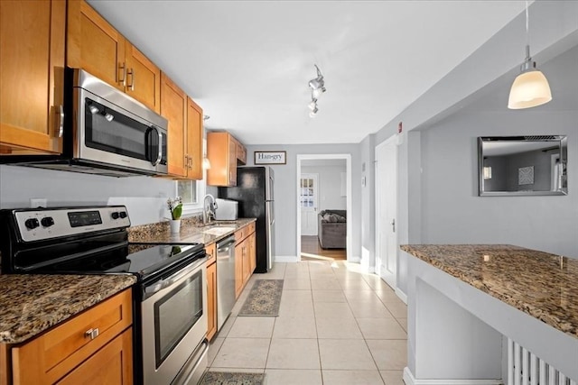 kitchen featuring dark stone countertops, appliances with stainless steel finishes, brown cabinets, light tile patterned flooring, and a sink