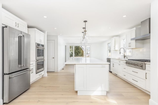 kitchen featuring a sink, appliances with stainless steel finishes, white cabinetry, wall chimney range hood, and tasteful backsplash