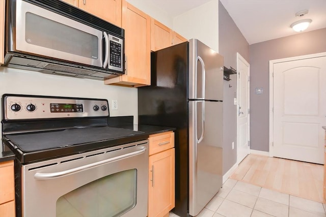kitchen featuring dark countertops, light brown cabinets, stainless steel appliances, baseboards, and light tile patterned floors