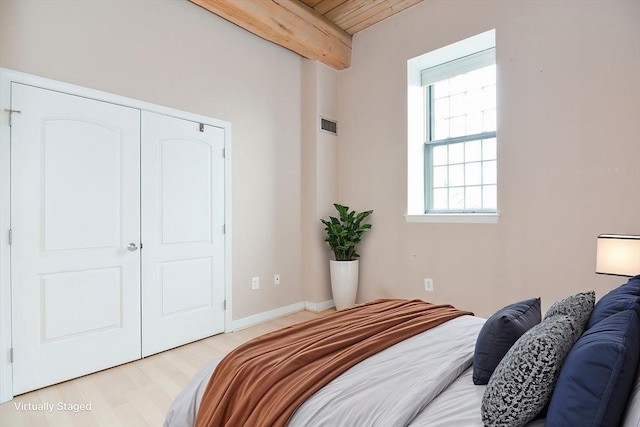 bedroom with visible vents, light wood-type flooring, wooden ceiling, beamed ceiling, and a closet
