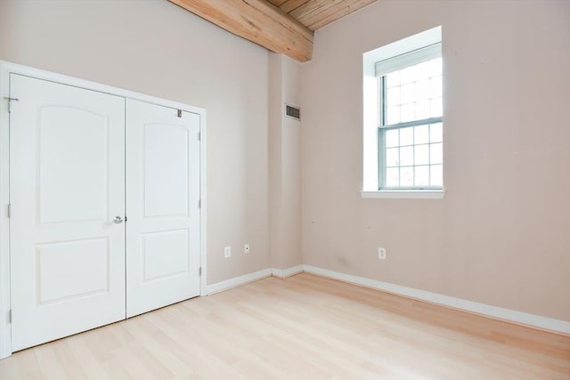 unfurnished bedroom with beamed ceiling, visible vents, baseboards, and light wood-style floors