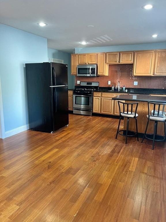 kitchen with dark countertops, backsplash, baseboards, wood finished floors, and stainless steel appliances