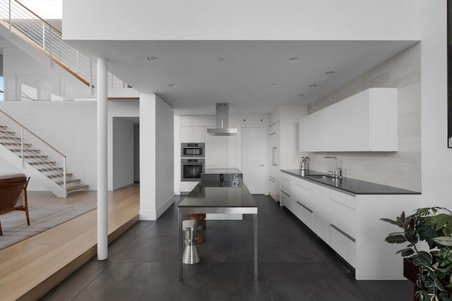 kitchen featuring wall chimney range hood, white cabinetry, sink, and stainless steel double oven