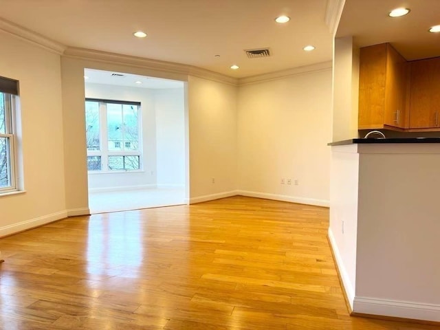 unfurnished living room with light wood-style floors, visible vents, ornamental molding, and baseboards