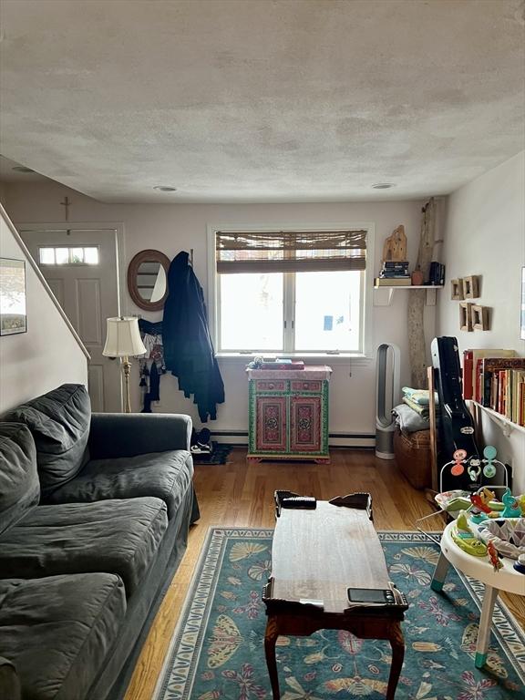 living room with wood-type flooring, a baseboard radiator, and a textured ceiling