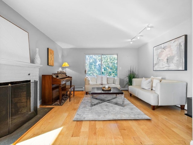 living area featuring a baseboard heating unit, baseboard heating, a brick fireplace, and wood finished floors