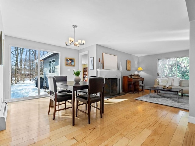 dining room featuring baseboard heating, a brick fireplace, a notable chandelier, and light wood finished floors