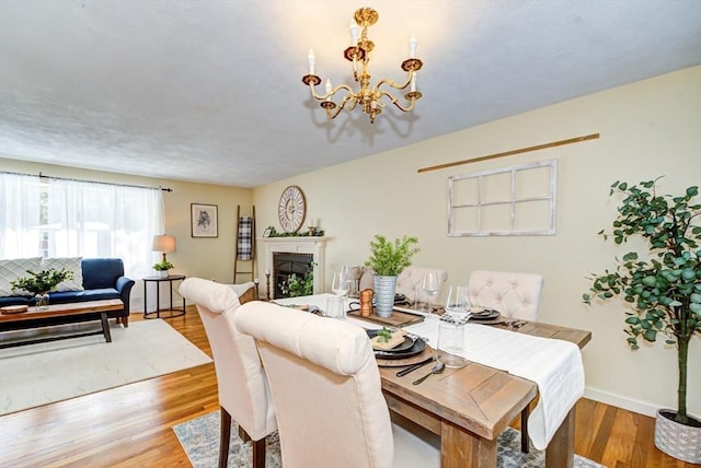 dining area with baseboards, light wood finished floors, a fireplace, and a notable chandelier