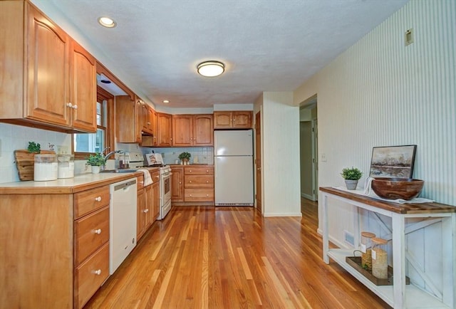 kitchen with tasteful backsplash, white appliances, light countertops, and light wood-style flooring