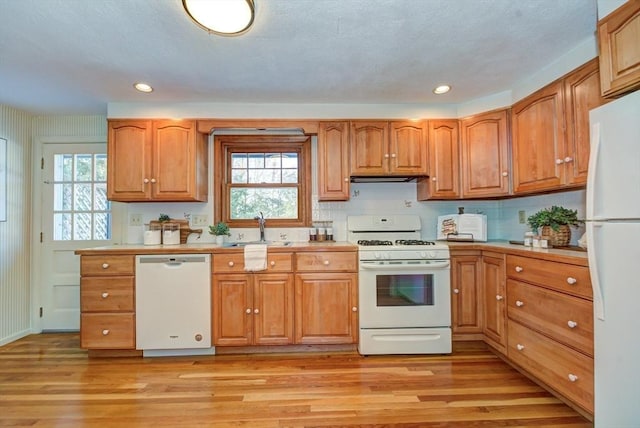 kitchen with brown cabinets, white appliances, light countertops, and a sink