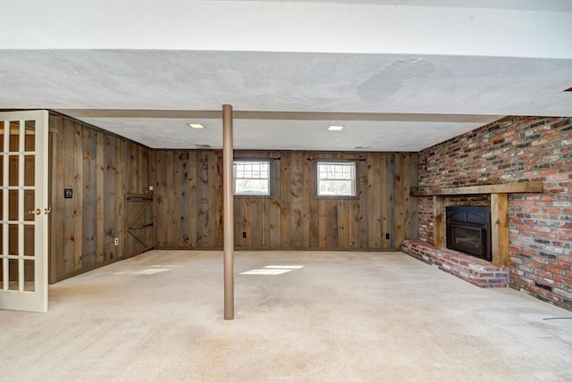 basement featuring carpet floors, a brick fireplace, and wooden walls