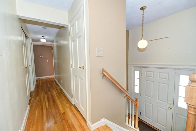 hall featuring light wood finished floors, baseboards, and an upstairs landing