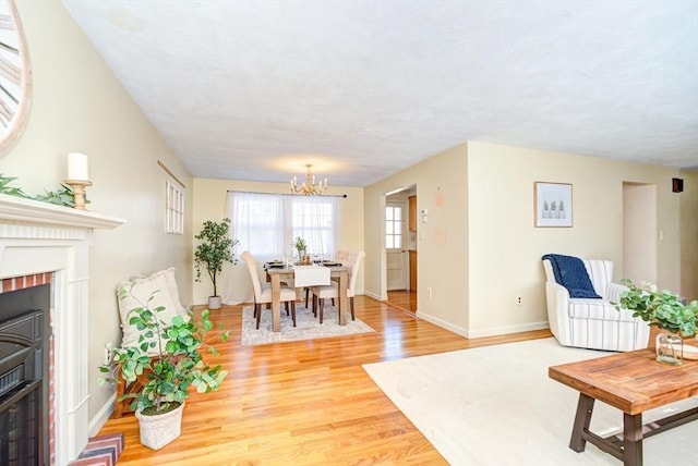 living room featuring a chandelier, light wood finished floors, a fireplace, and baseboards