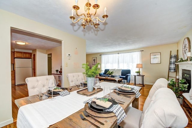 dining area with a glass covered fireplace, baseboards, light wood finished floors, and an inviting chandelier