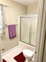bathroom with a shower with shower door, tile patterned flooring, toilet, and baseboards