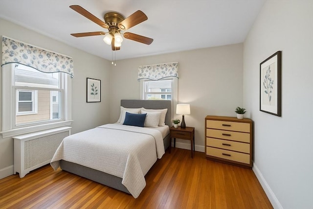 bedroom featuring a ceiling fan, baseboards, wood finished floors, and radiator