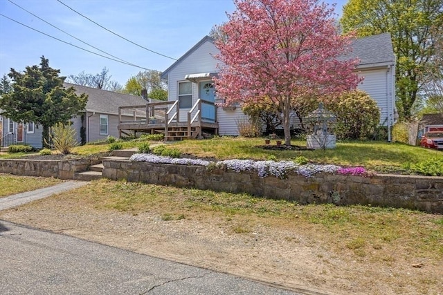 view of property hidden behind natural elements featuring a wooden deck and a front yard