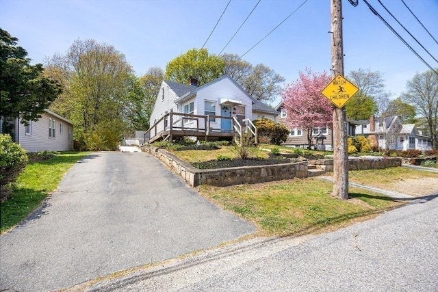exterior space featuring driveway, a wooden deck, and a front lawn