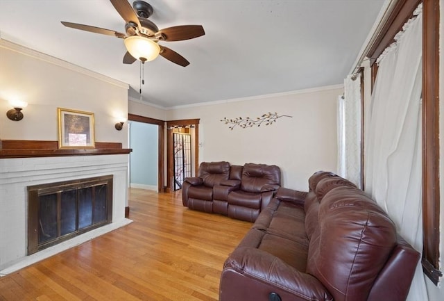 living area featuring ornamental molding, a fireplace, baseboards, a ceiling fan, and light wood-style flooring