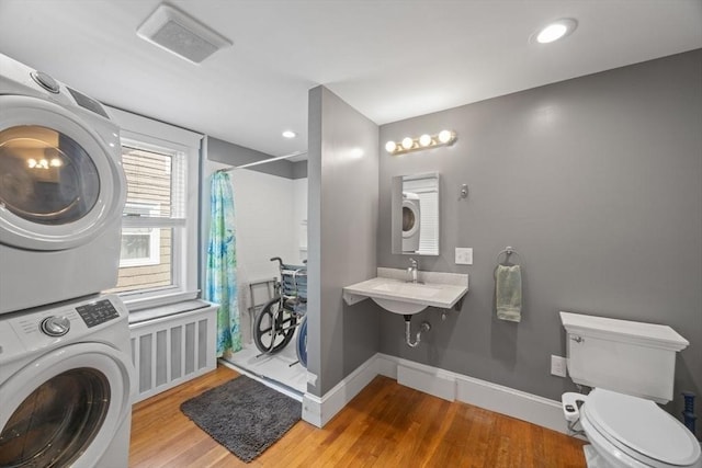 bathroom featuring wood finished floors, stacked washer / drying machine, toilet, and curtained shower