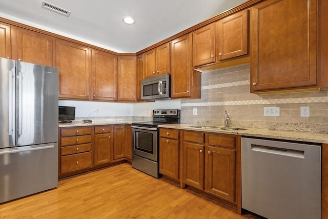 kitchen featuring stainless steel appliances, sink, light hardwood / wood-style floors, and light stone countertops