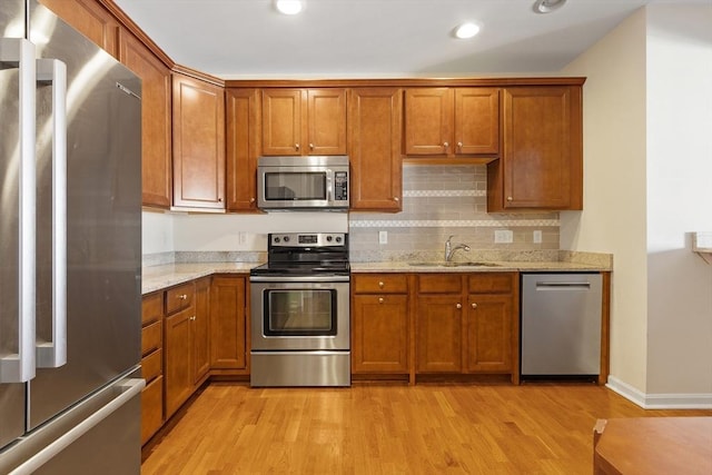 kitchen with stainless steel appliances, light stone countertops, light hardwood / wood-style flooring, and sink