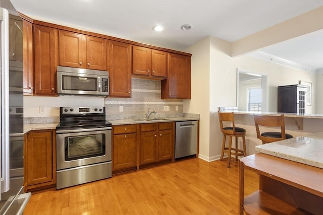 kitchen with appliances with stainless steel finishes, light stone counters, sink, light hardwood / wood-style flooring, and tasteful backsplash