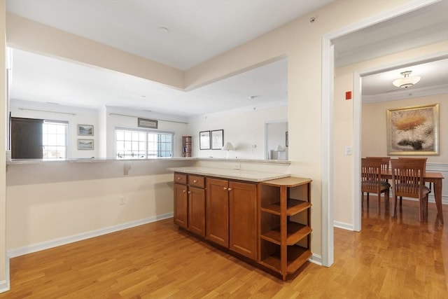 kitchen with light stone counters, kitchen peninsula, light wood-type flooring, and ornamental molding