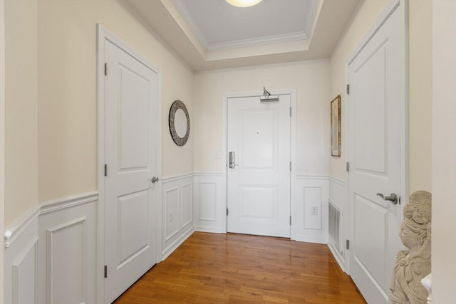 doorway with hardwood / wood-style flooring, a raised ceiling, and crown molding