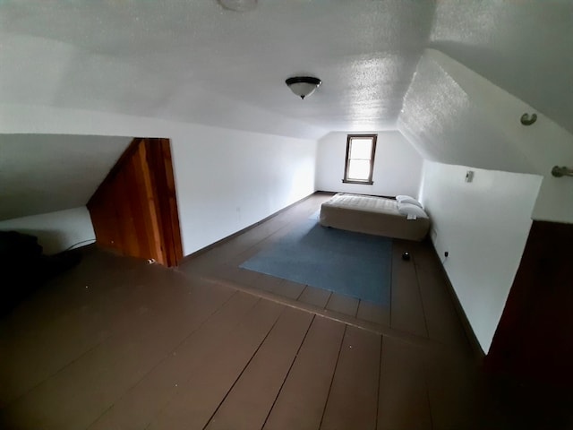 additional living space featuring a textured ceiling, vaulted ceiling, and hardwood / wood-style flooring