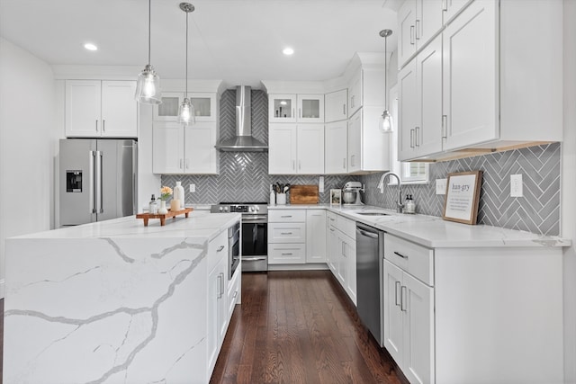 kitchen with sink, white cabinets, hanging light fixtures, wall chimney range hood, and appliances with stainless steel finishes