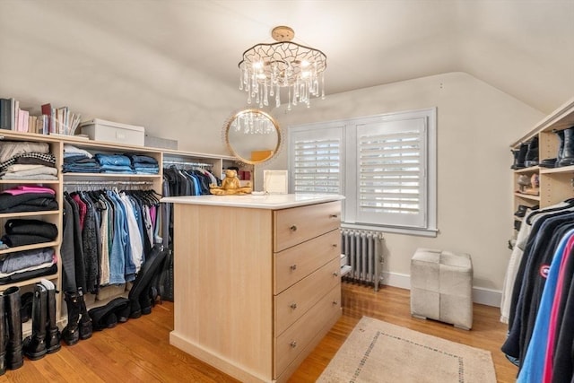 walk in closet with lofted ceiling, a notable chandelier, radiator heating unit, and light wood finished floors